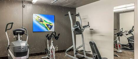 Un gimnasio con equipo de ejercicio, un espejo grande y un televisor montado en la pared.