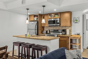A modern kitchen with a central island, bar stools, a wooden bar, and a stone backsplash.