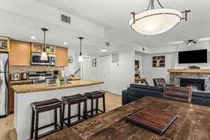 A modern kitchen with a central island, bar stools, a dining table, and a fireplace.