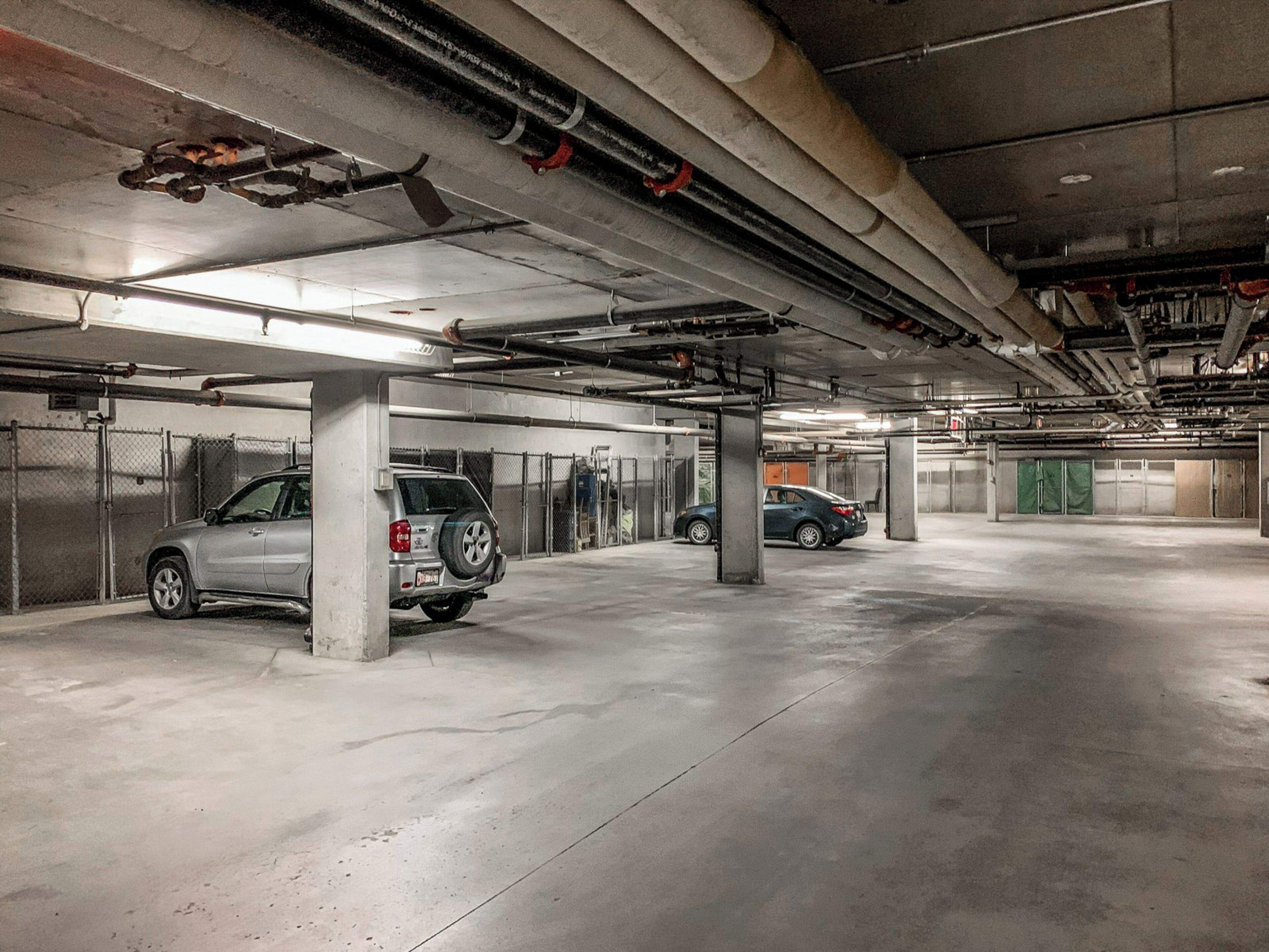 A multi-level parking garage with concrete pillars, metal railings, and overhead pipes.