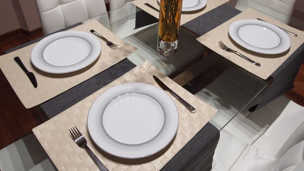 Une table à manger dressée pour quatre personnes, avec de l’assiette blanche, des couverts et un vase rempli de fleurs.