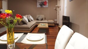 Un salon moderne avec un canapé, une table basse et une table à manger, cette dernière étant dressée avec des assiettes et un vase rempli de fleurs.