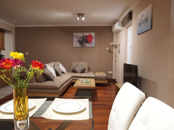 A modern living room with a sofa, a coffee table, and a dining table set with plates and a vase of flowers.