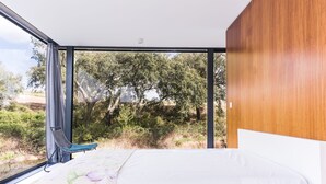 A bedroom with a large window, a bed, a chair, and a view of trees and hills. - Bungalow 2 - Montemor (Foros de Vale Figueira)