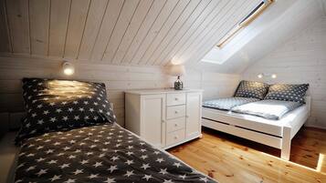 Ein Schlafzimmer mit schrägem Dach, einem Oberlicht, einem Bett mit sternenmusternder Bettwäsche, einem Nachttisch mit Lampe und einer weißen Kommode.