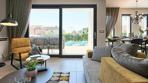 A modern living room with a sofa, armchairs, a coffee table, and a dining area with a view of a swimming pool and greenery. - Beautiful private villa for 8 guests with hot tub, private pool, WIFI, A/C, TV and terrace (Umag)