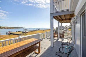 A wooden deck with a bench and chairs overlooking a beach and water.