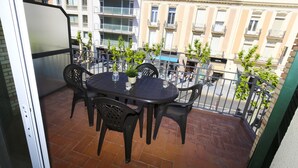 En balkon med et bord og stole, med udsigt over en gade med bygninger og et hotelskilt.