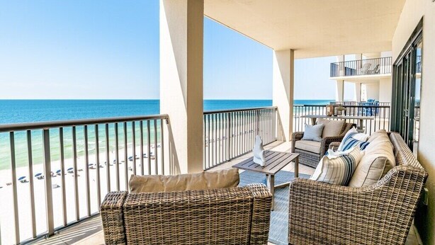 A balcony with wicker furniture, a table, and a view of the beach and ocean.