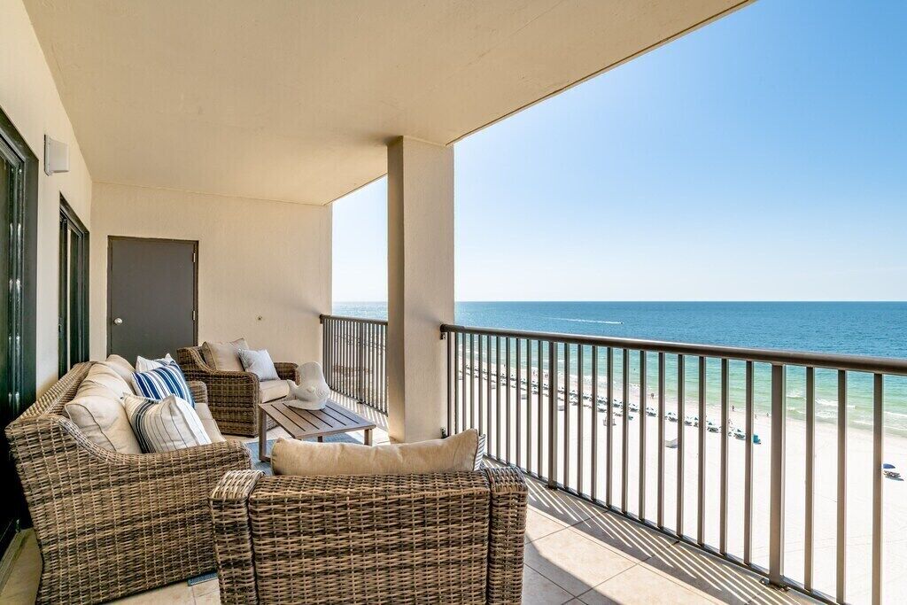 A balcony with wicker furniture and a view of the beach.