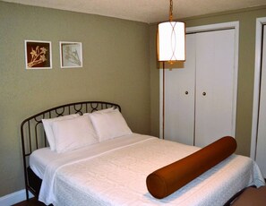 A neatly made bed with a white comforter and pillows, a wooden headboard, and a hanging light fixture above. - Prairie Comfort  Your Peaceful, Private & Affordable Retreat (Grand Forks)