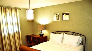 Una habitación de hotel con cama, mesita de noche, lámpara y ventana con cortinas.