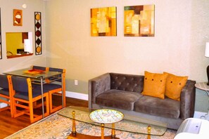Un salon comprenant une table à manger avec un plateau en verre, un canapé en cuir capitonné et un tapis à motifs.