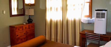 Una habitación de hotel con una cama, un aparador, un escritorio con silla, un calentador portátil y una ventana con cortinas.