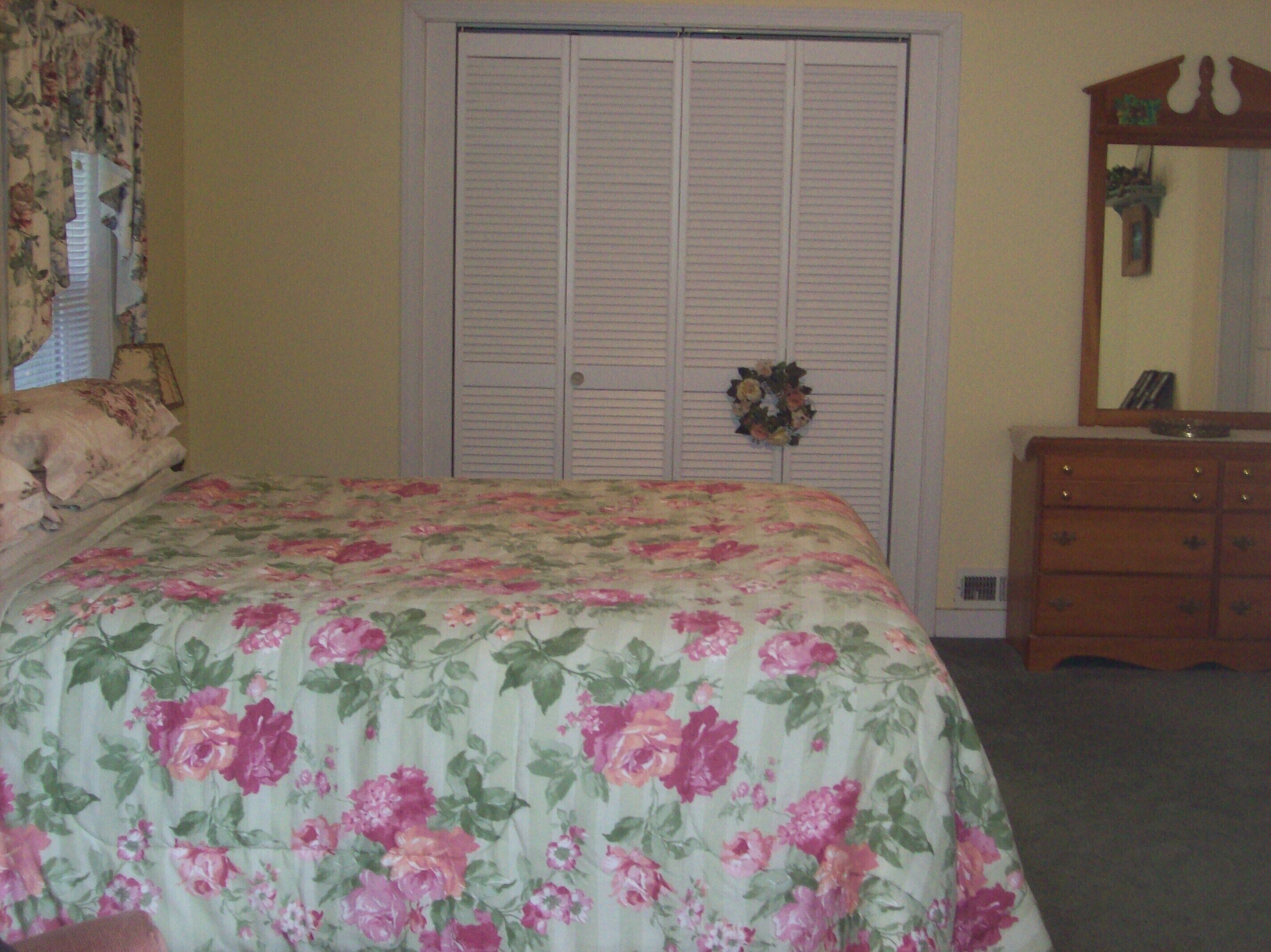 A bedroom with a floral bedspread, a wardrobe with a mirror, and a dresser.