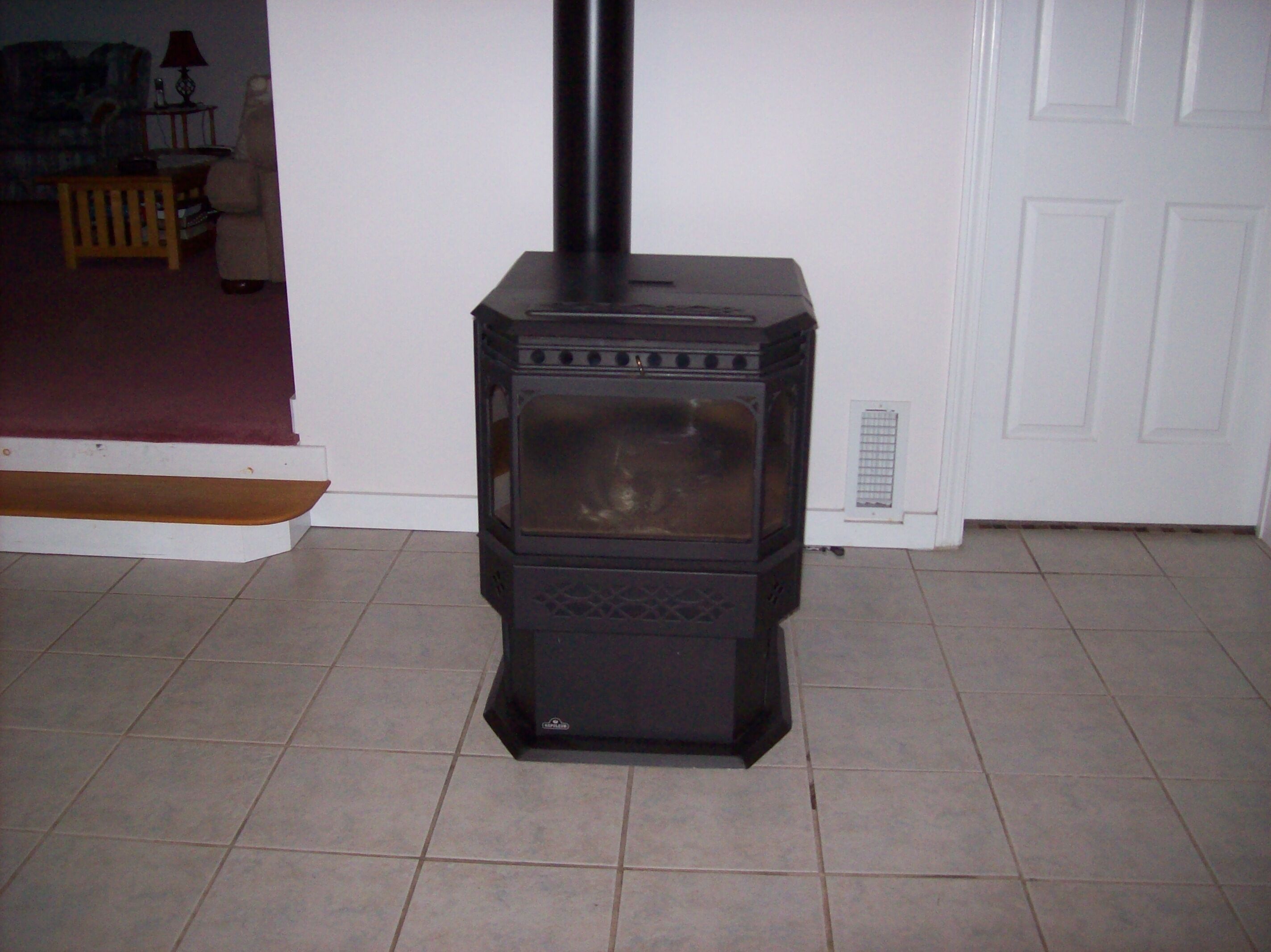 A black wood-burning stove in a room with tiled flooring and a white door.
