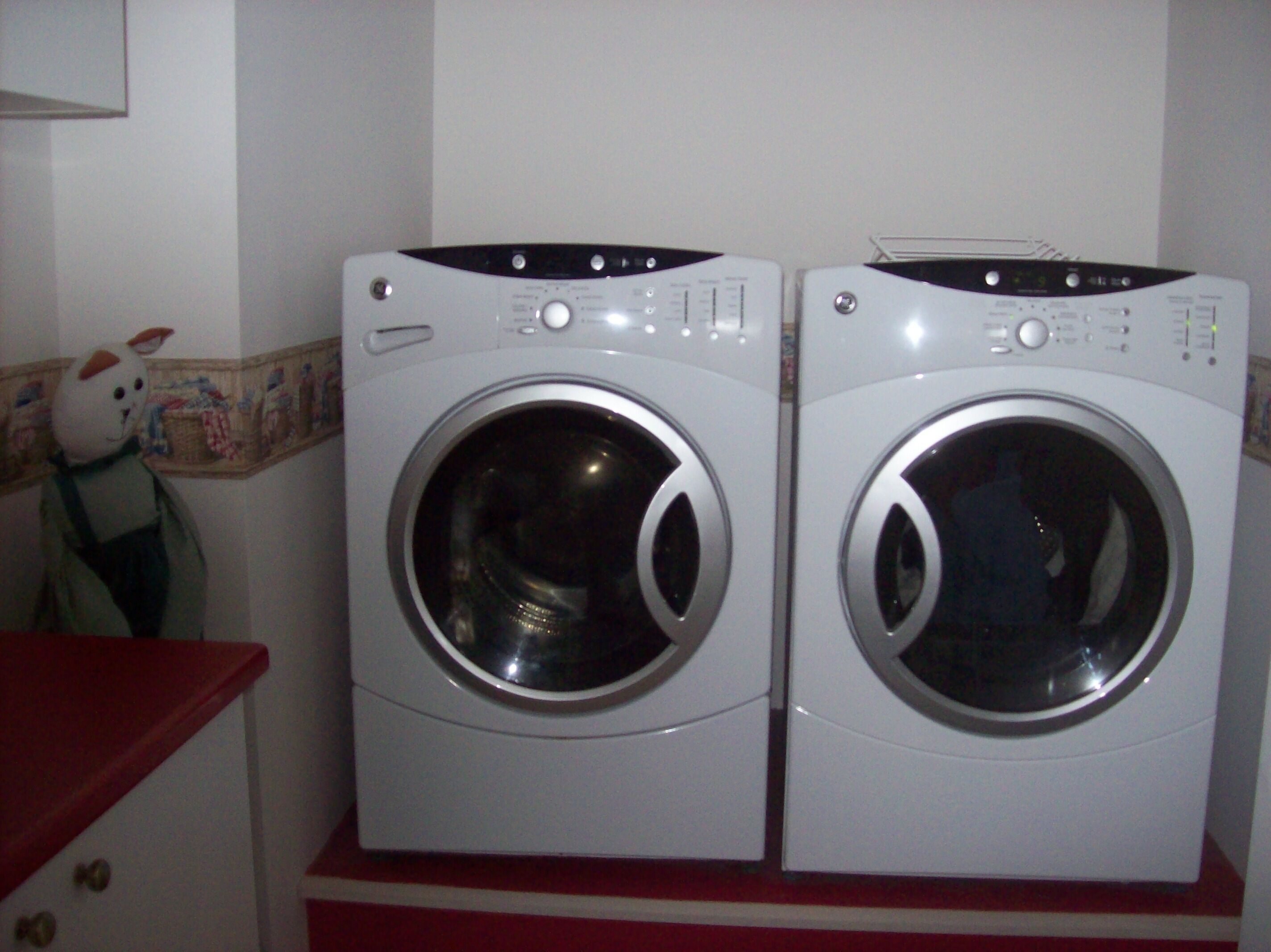 Two front-loading washing machines in a laundry room with a red countertop and a decorative wall piece.
