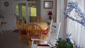 A dining area with a wooden table and chairs, a chandelier, and a view through the glass door. - Light Oak Leaf Cottage (Bar Harbor)