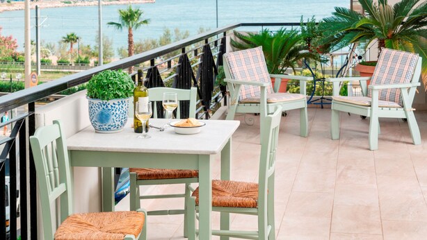 A balcony with a table and chairs, a potted plant, and a view of the sea. - Unique flat with Sea view by Athenian Home, Athenian Homes (Paleo Faliro)