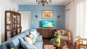 A living room with a blue sofa, a wooden cabinet, a television, and a patterned rug. - Unique flat with Sea view by Athenian Home, Athenian Homes (Paleo Faliro)