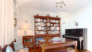 A living room with a wooden bookshelf, a glass-top coffee table, a sofa, a piano, and a patterned rug. - Unique flat with Sea view by Athenian Home, Athenian Homes (Paleo Faliro)