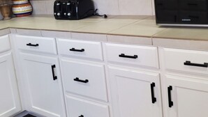 Una cocina con armarios blancos, pomos negros, un tostador y un microondas.