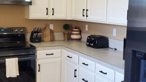 Una cocina con armarios blancos, una estufa negra, un tostador y un refrigerador.