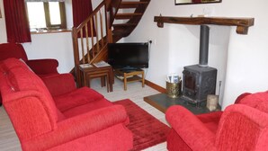 A living room with red sofas, a wooden staircase, a television, and a wood-burning stove.