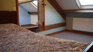 A bedroom with a patterned bedspread, a skylight, a wooden staircase, and a radiator.