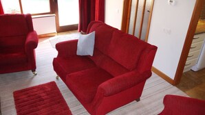 A red sofa with a white pillow, a red rug, and a wooden floor.