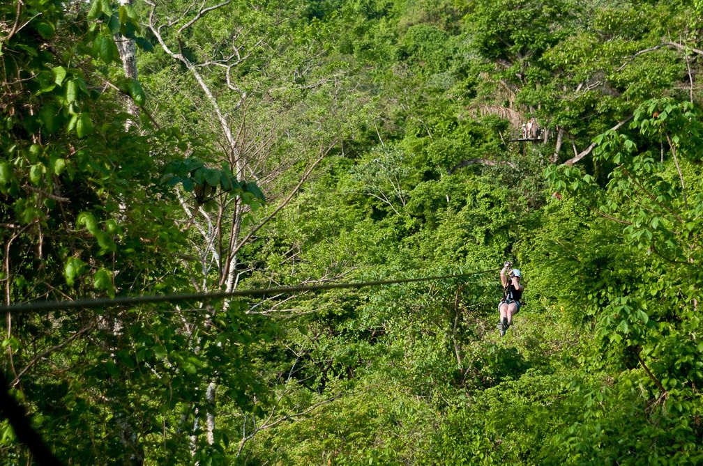 Iemand beleeft een zipline-avontuur door een dicht, groen bos.