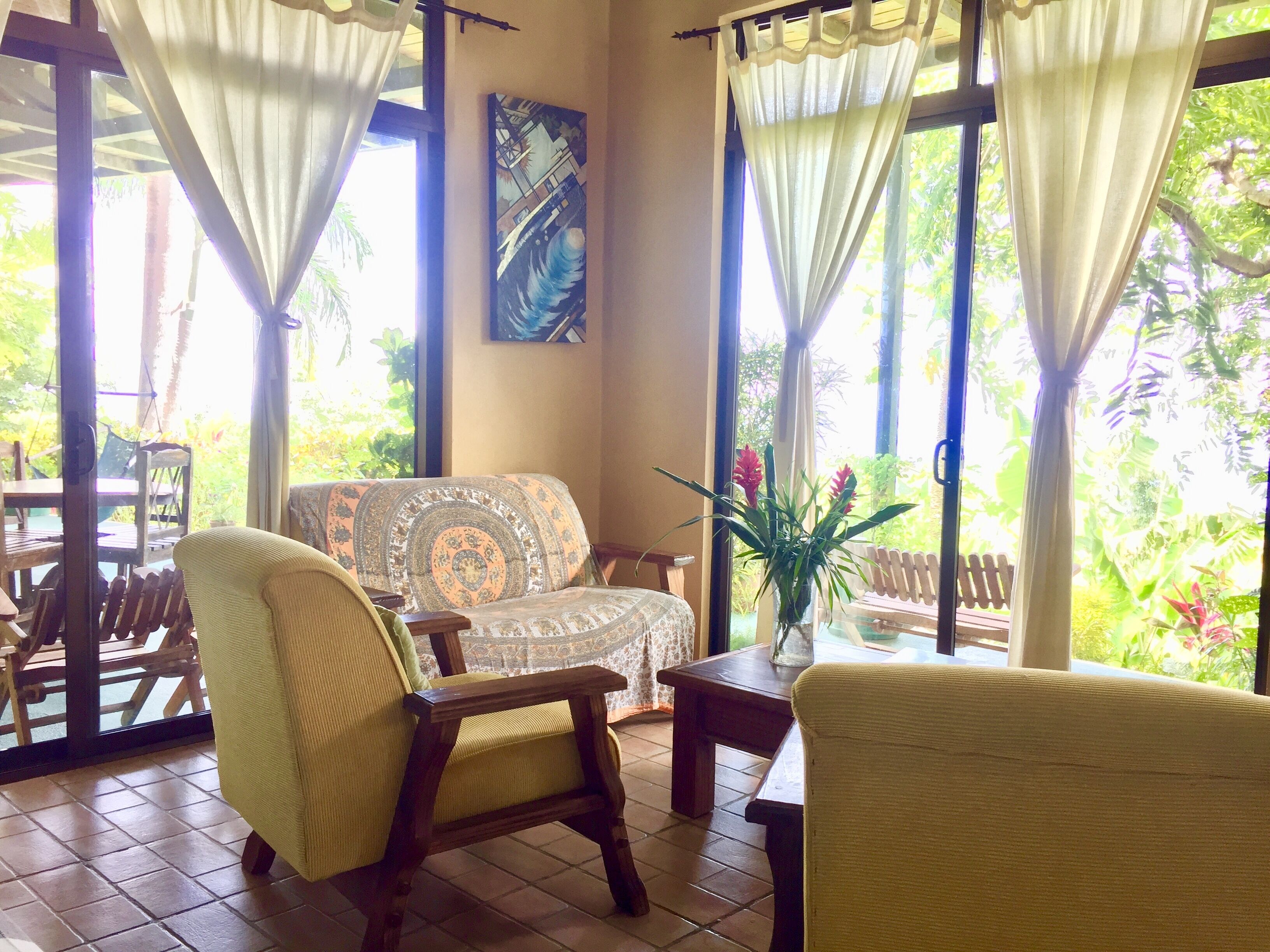 A room with a patterned sofa, a wooden chair, a small table, and a potted plant.