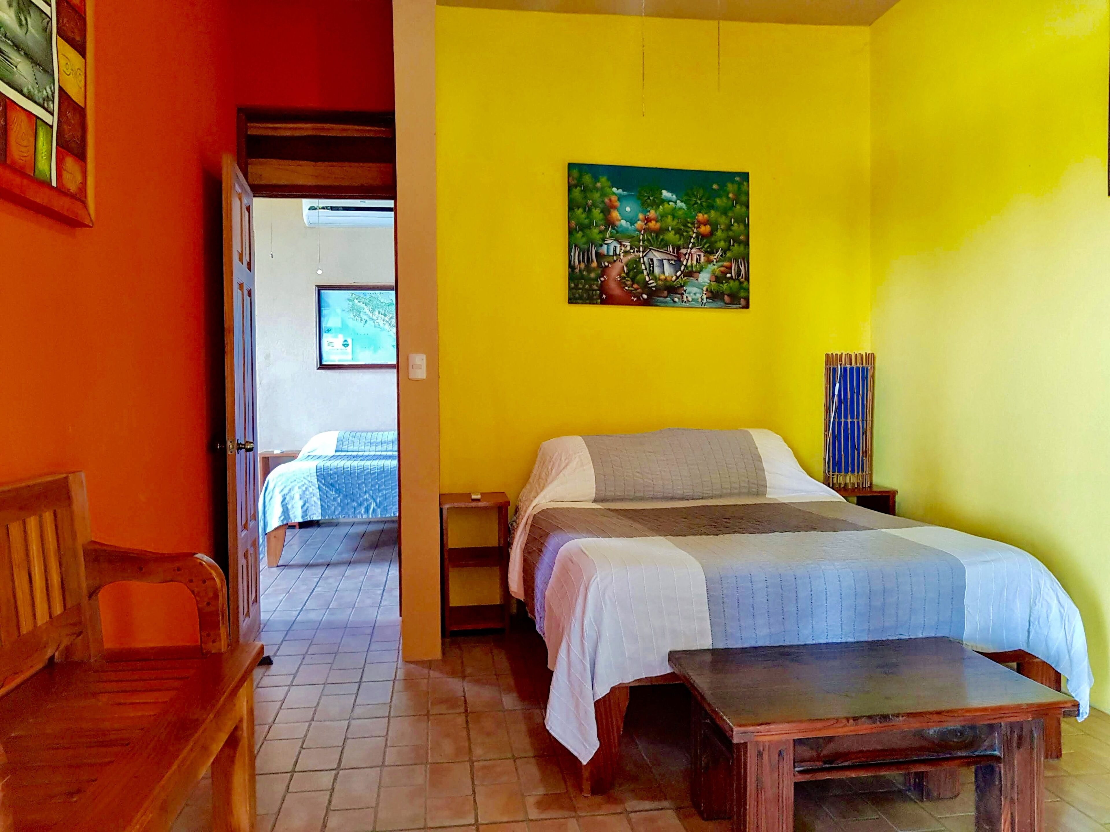 Una habitación con una cama, un banco de madera, una mesita y un cuadro en la pared.