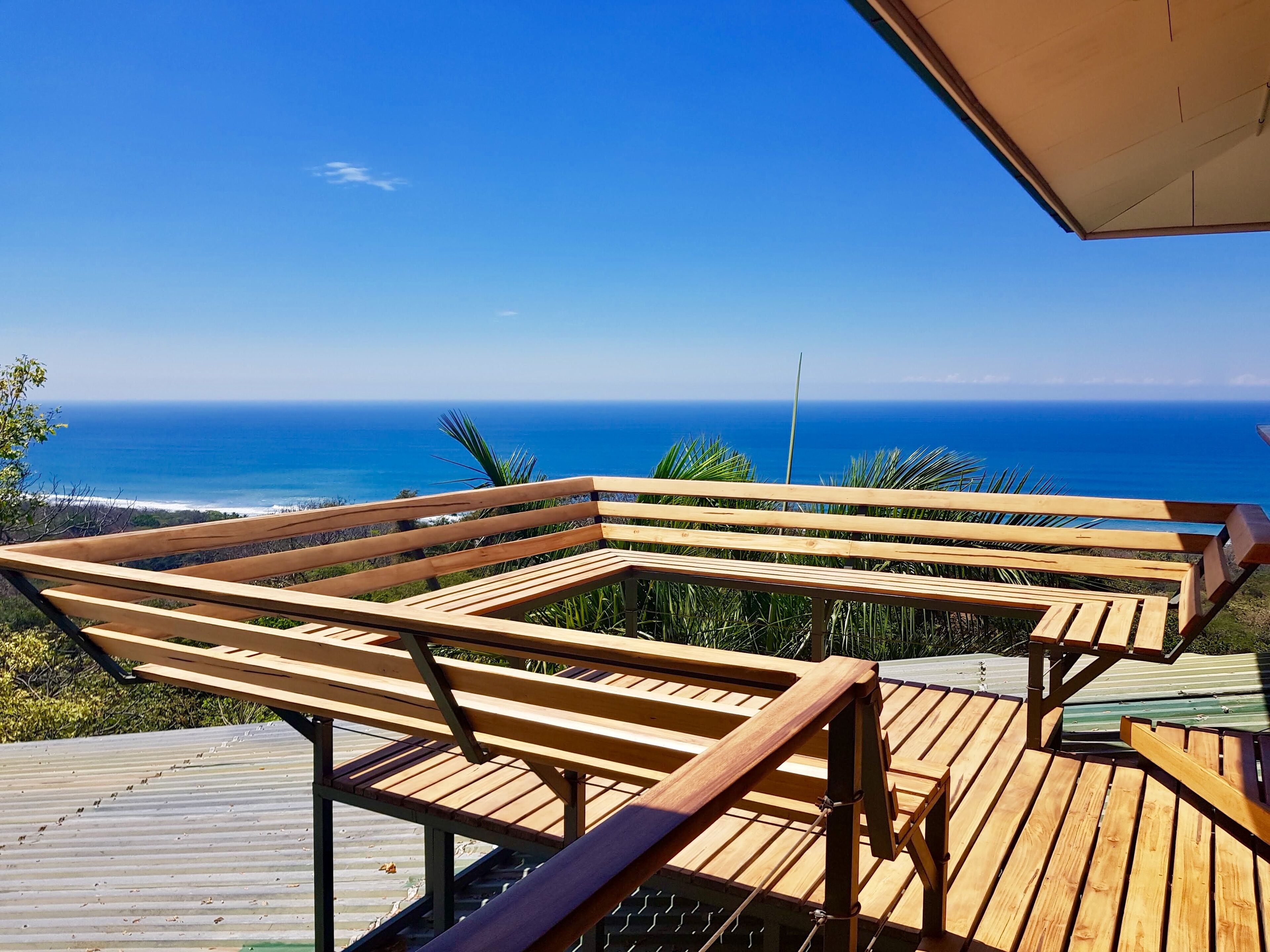A wooden deck with a bench overlooking a coastal view.