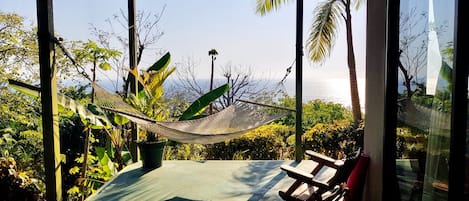 A hammock on a porch with a view of the ocean.