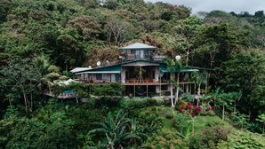 Ein zweistöckiges Haus mit Balkon, umgeben von dichtem Wald.