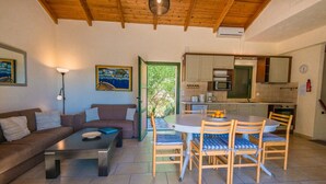 Una sala de estar acogedora con un sofá, una mesa de centro y un comedor con sillas y una mesa. Se observa una cocina con alacenas y electrodomésticos.