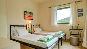 Una habitación con dos camas, una mesita con una lámpara, una ventana con cortinas y vistas a la montaña.