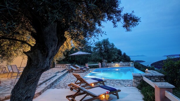 Zona de piscina con sillones reclinables, terraza de piedra y vista al mar.