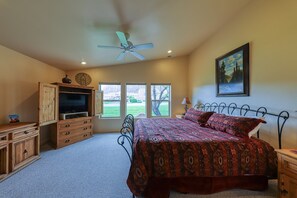 A bedroom with a bed, a TV, wooden furniture, and a painting on the wall. - Lovely Townhome with Seasonal Shared Pool and Hot Tub and Mountain Views (Moab)