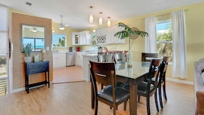 A modern kitchen with white cabinets, a dining table with chairs, and a large window with curtains. - Welcome to Villa Rosa! A 4 Bedroom 3 Bath Oceanfront Getaway (St. Augustine)