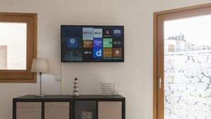Ein Wohnzimmer mit Flachbildfernseher an der Wand, der verschiedene Streaming-Dienste anzeigt.