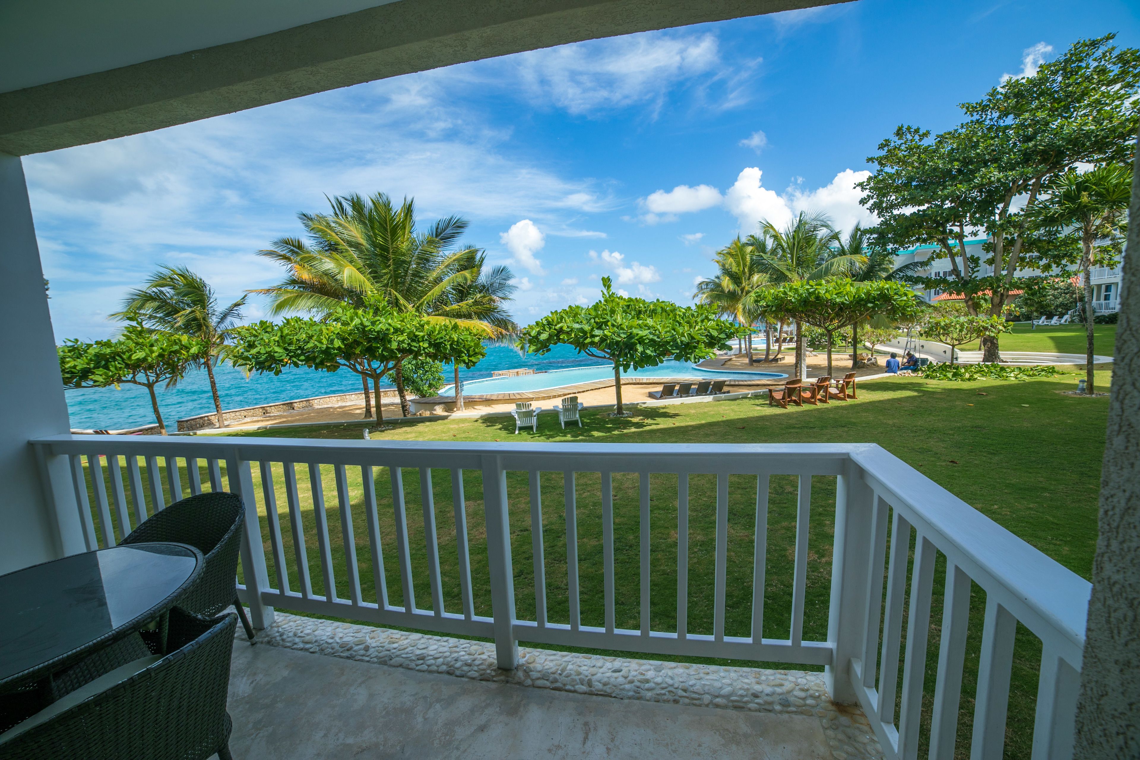 A balcony with a view of a pool, palm trees, and a beach.