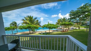 A balcony with a view of a pool, palm trees, and a beach. - Whispering Seas (Tower Isle)