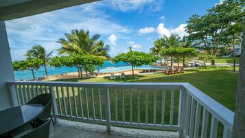 A balcony with a view of a pool, palm trees, and a beach.