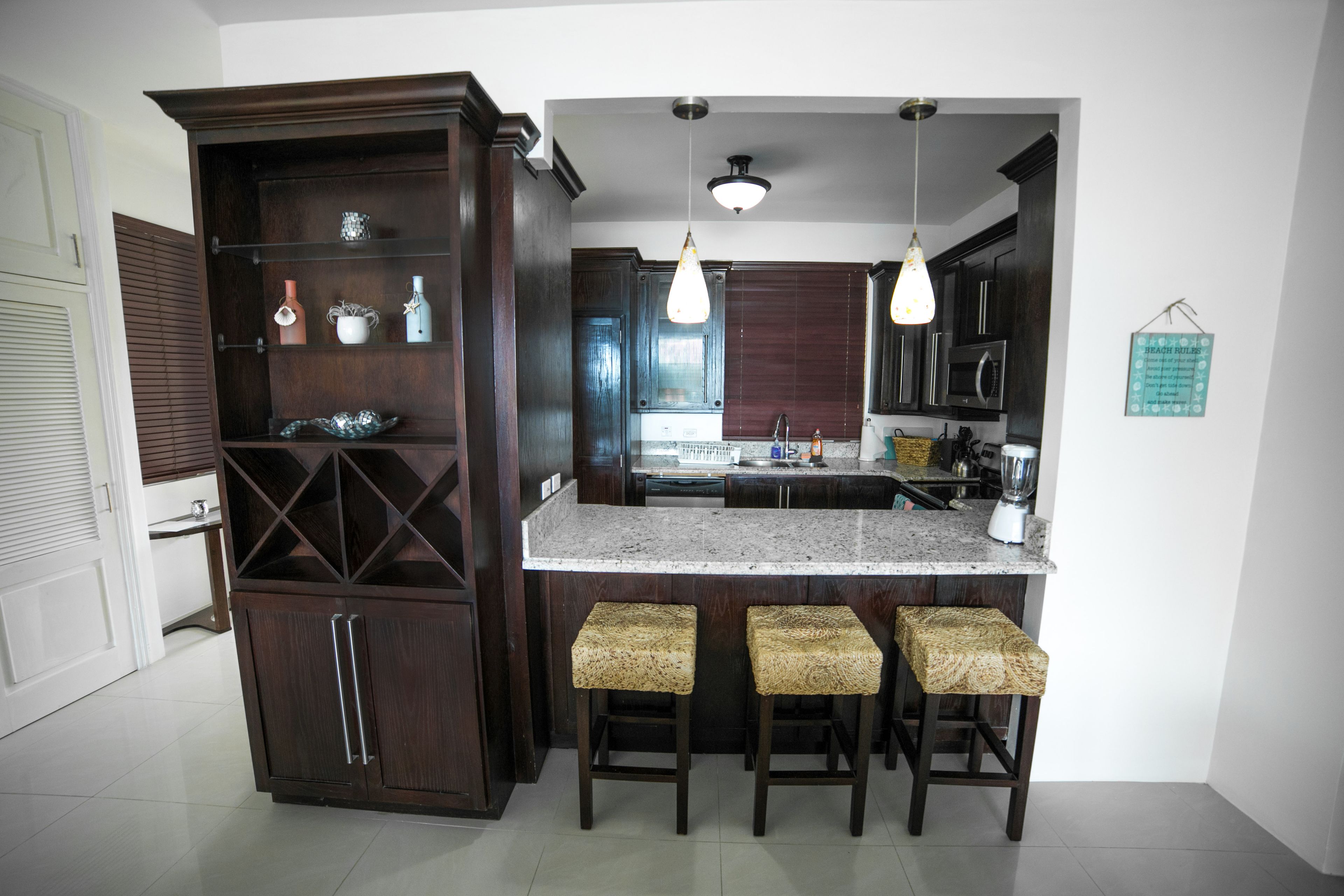 A kitchen with dark wood cabinets, a granite countertop, and three woven stools.