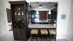 A kitchen with dark wood cabinets, a granite countertop, and three woven stools. - Whispering Seas (Tower Isle)