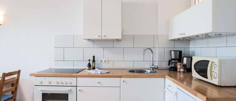 A compact kitchen with white cabinets, a wooden countertop, a built-in oven, a microwave, and a coffee maker.