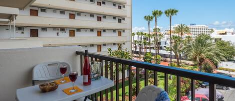 A balcony with a table set for two, a bottle of red wine, and a bowl of nuts.