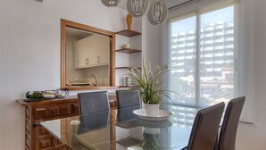 A dining area with a glass table, four chairs, a potted plant, and a wooden cabinet with a mirror above it. - Cosy apartment for 4 people with pool, A/C, WIFI, TV and terrace (Benissa)